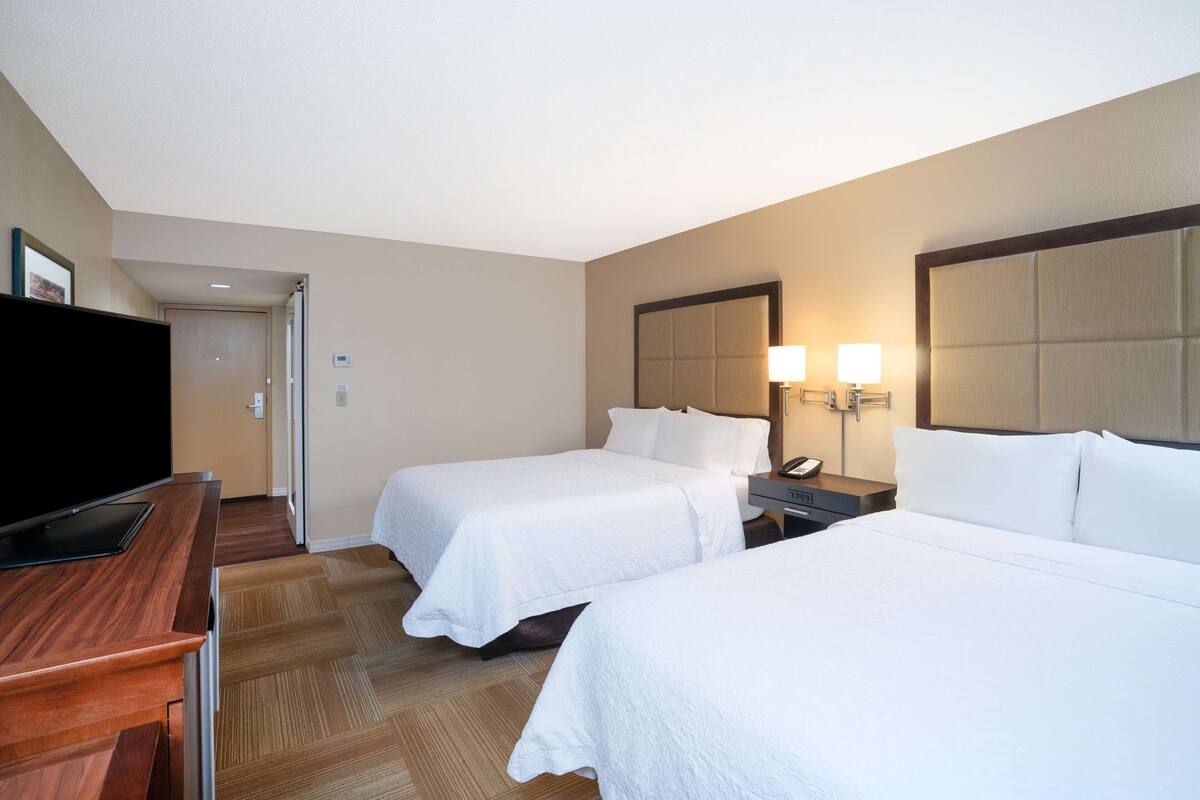 A hotel room with two beds, a TV, a desk, and a mirror.