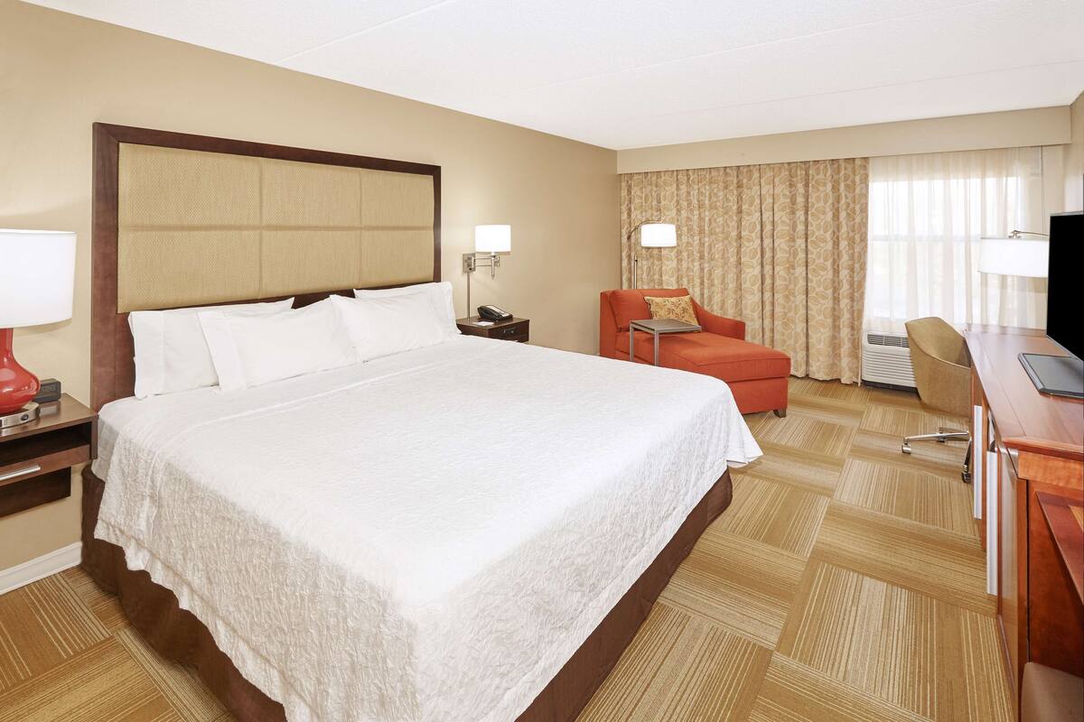 A hotel room with a large bed, a desk with a chair, a television, and a desk lamp.