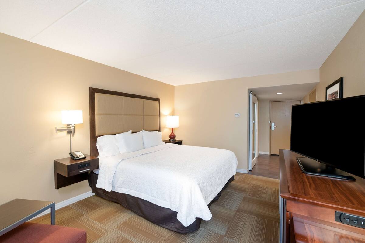 A hotel room with a bed, bedside lamps, a TV, and a desk.