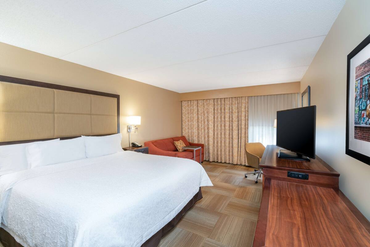 A hotel room with a large bed, a sofa, a TV, and a desk.