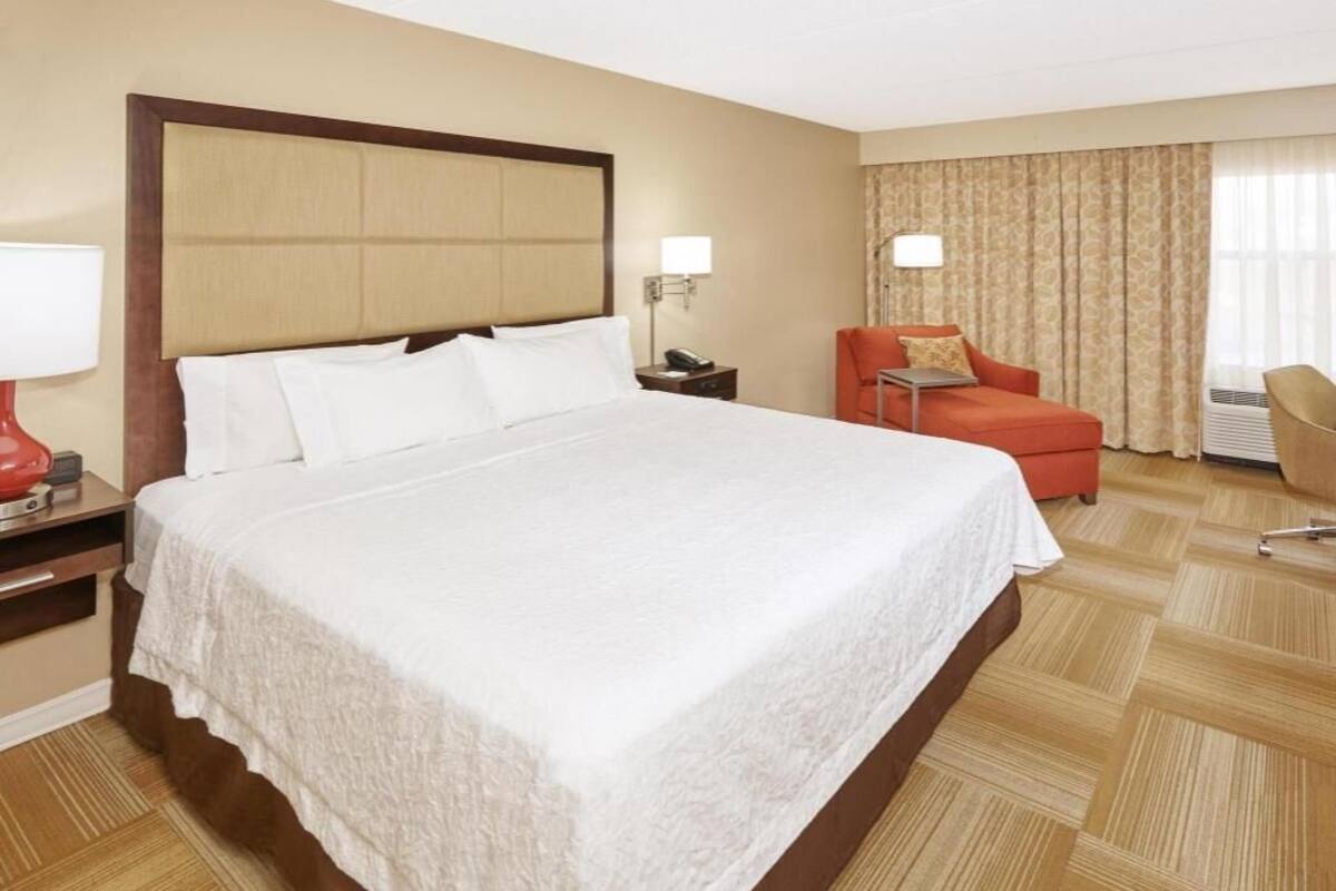 A hotel room with a large bed, a desk, a chair, and a desk lamp.