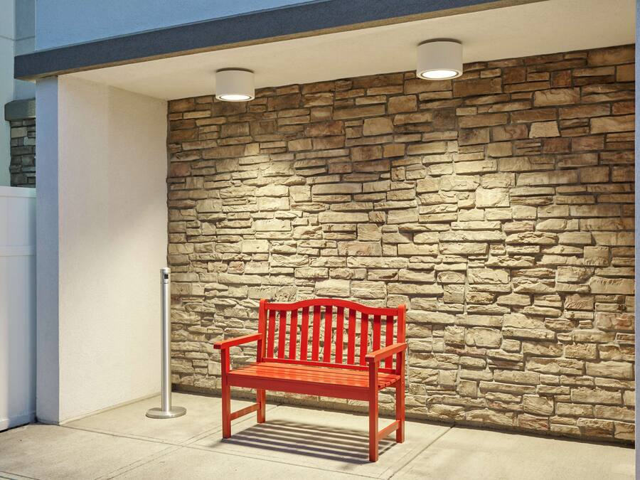 Eine rote Bank vor einer Steinmauer mit weißem Zaun und einem Metallpfosten.