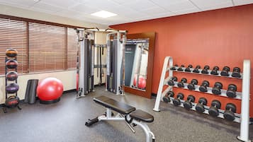 A gym with a bench, dumbbells, a medicine ball, and a wall-mounted squat rack.