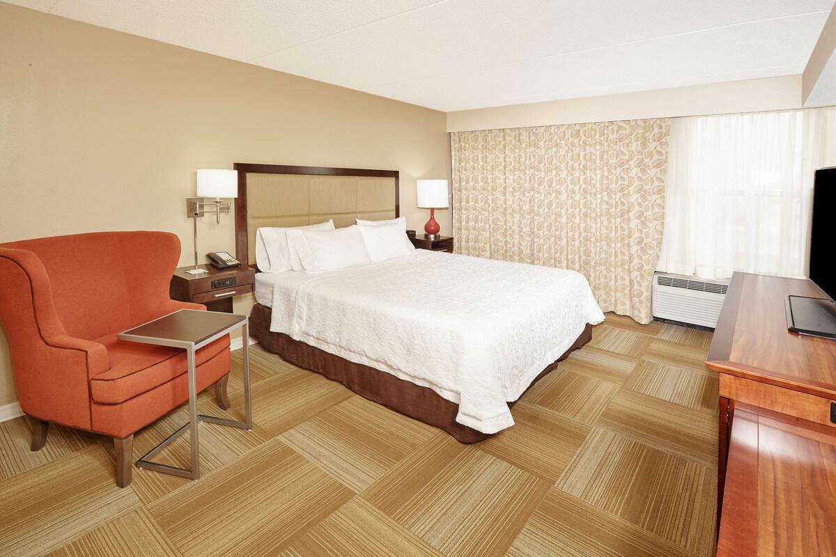 A hotel room with a bed, a desk, a chair, a TV, and a window with curtains.