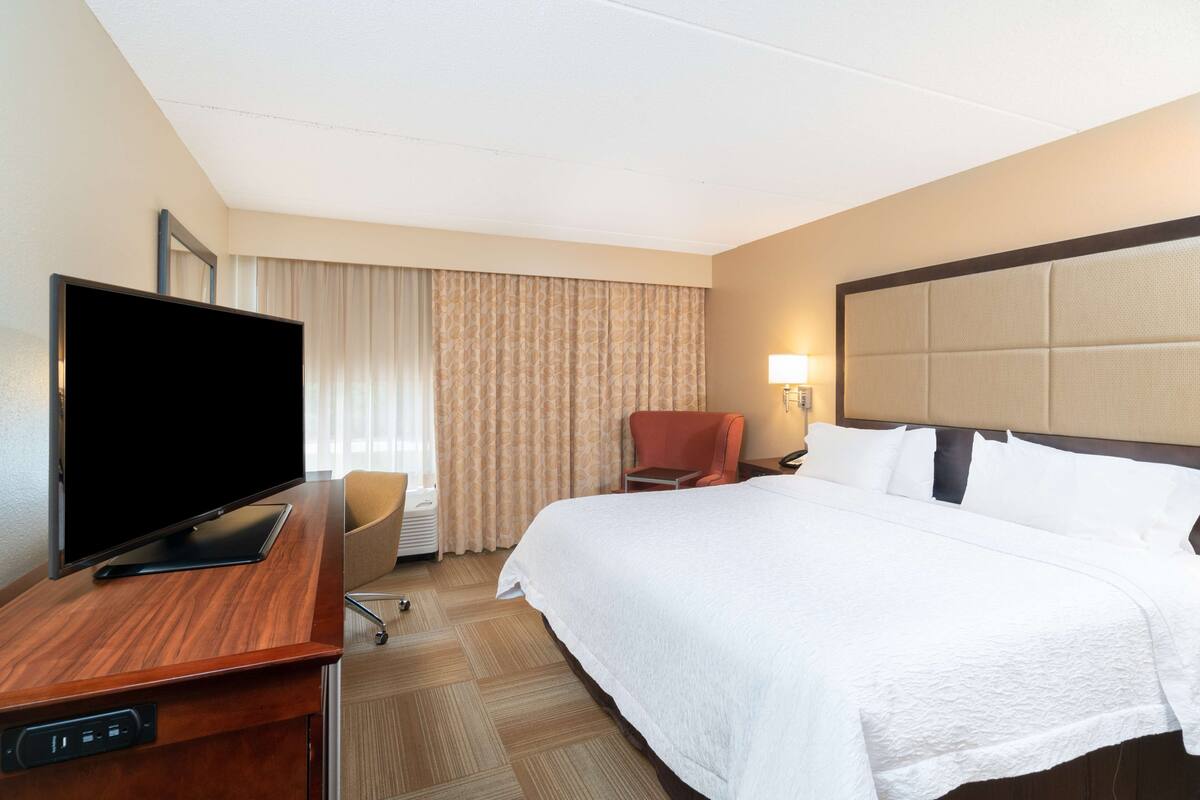A hotel room with a bed, a television on a desk, a chair, and a lamp.