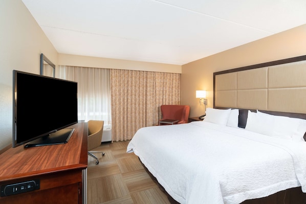 Una habitación de hotel con cama, televisión sobre un escritorio, una silla y una lámpara.