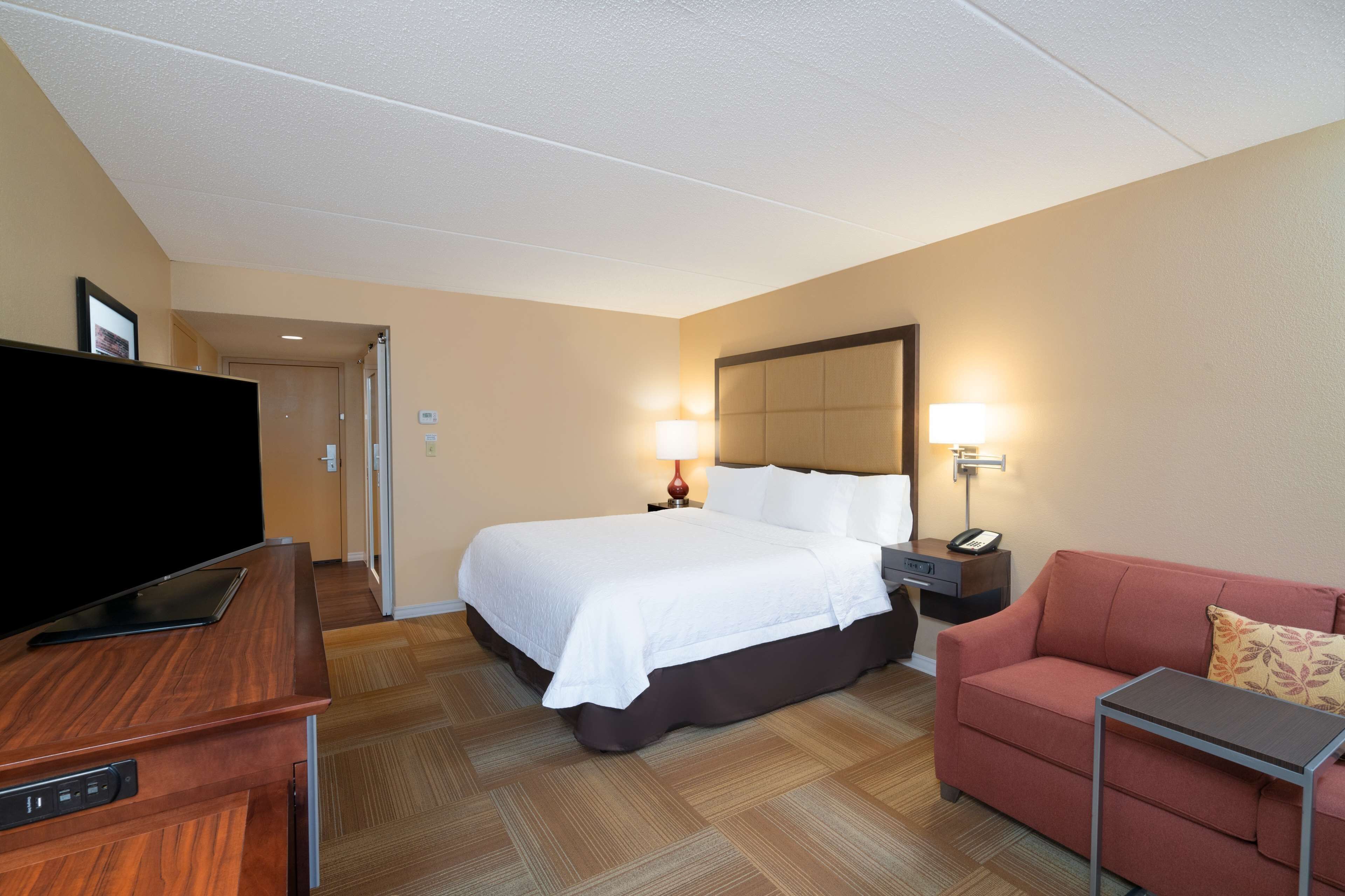A hotel room with a bed, a TV, a desk, a chair, and a sofa.
