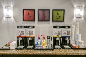 A coffee station with multiple coffee dispensers labeled '100% Arabica Bean Coffee' and 'Decaf Roast'. There are also condiment dispensers and a stack of disposable cups. - Hampton Inn & Suites Memphis-Wolfchase Galleria (Memphis)