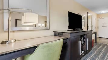 Una habitación de hotel con escritorio, televisor, espejo y puerta.