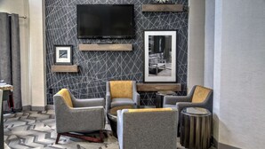 Un área de estar moderna con sillones tapizados en gris, una mesa redonda de centro y un televisor de pantalla plana montado en la pared.
