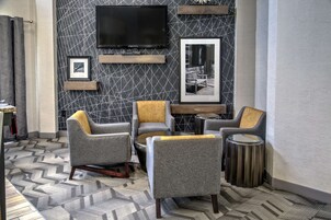 Ein moderner Lounge-Bereich mit grauen Polstersesseln, einem runden Couchtisch und einem an der Wand befestigten Flachbildfernseher.
