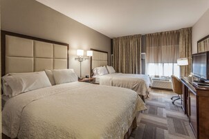 Una habitación de hotel con dos camas, un escritorio con televisor y un ventanal con cortinas.