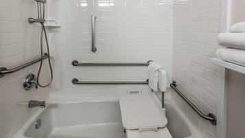 Un baño con bañera, barras de apoyo, cabezal de ducha y un perchero para toallas.