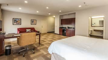 Habitación de hotel con una cama grande, un escritorio con una silla, una kitchenette y un baño.