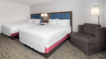 A hotel room with two beds, a nightstand, a lamp, and a sofa.