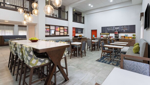 A spacious dining area with high ceilings, modern pendant lighting, and a variety of seating options including tables and chairs.