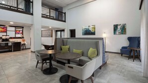 A modern lobby with a seating area featuring a sofa and two round tables, a staircase, and artwork on the walls.