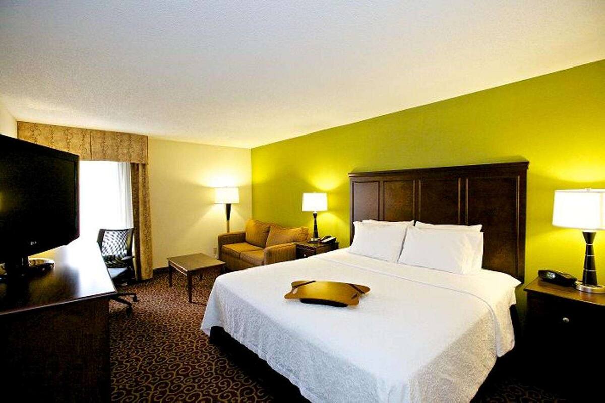 A hotel room with a large bed, two bedside lamps, a television, a desk, and a chair.