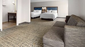 A hotel room with two beds, a sofa, a small table, and a bathroom visible through an open door.