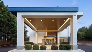 A modern hotel entrance with a covered outdoor area, a reception desk, and a clear sky.