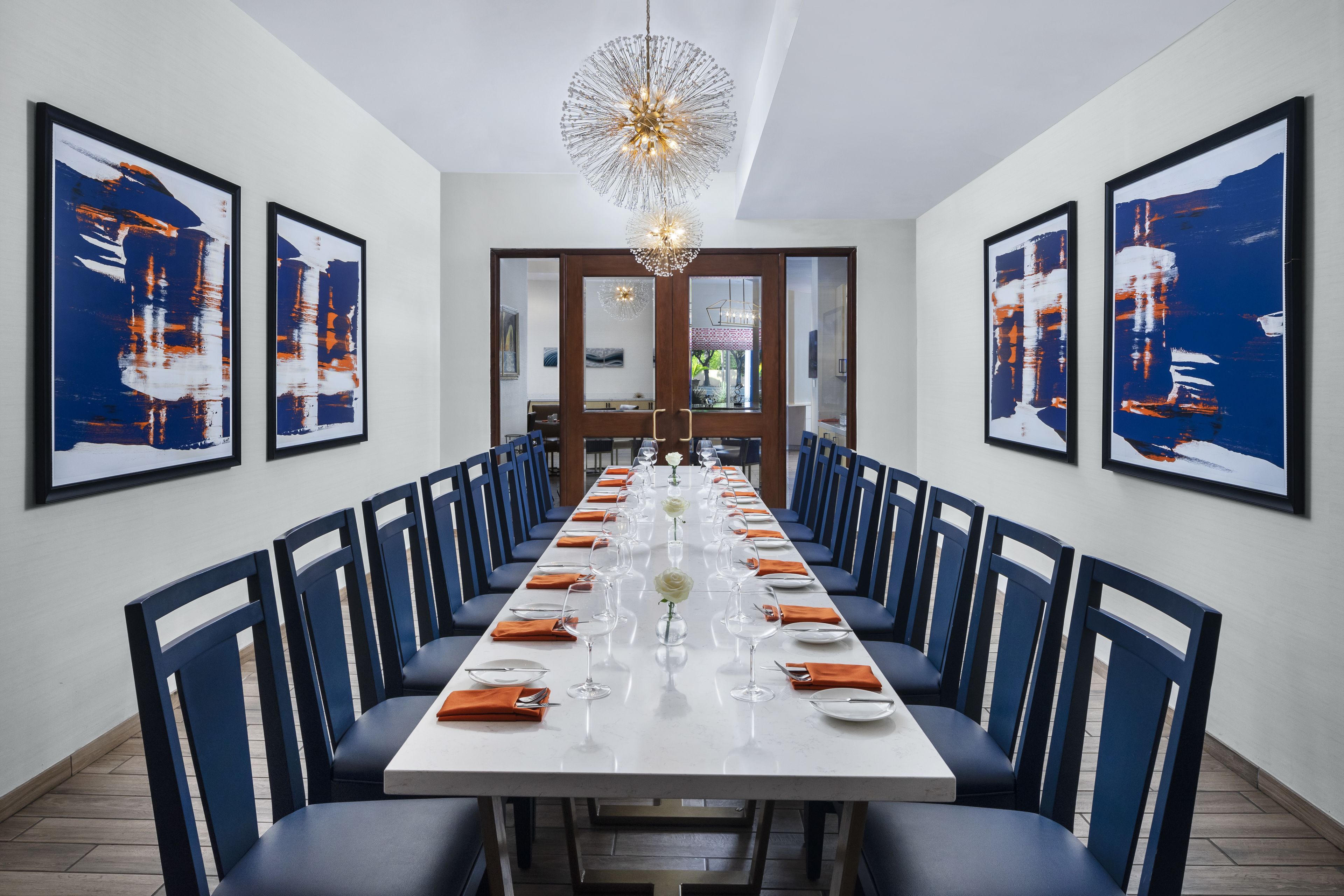 A long dining table with blue chairs, white tablecloth, and a chandelier.