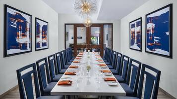 A long dining table with blue chairs, white tablecloth, and a chandelier.