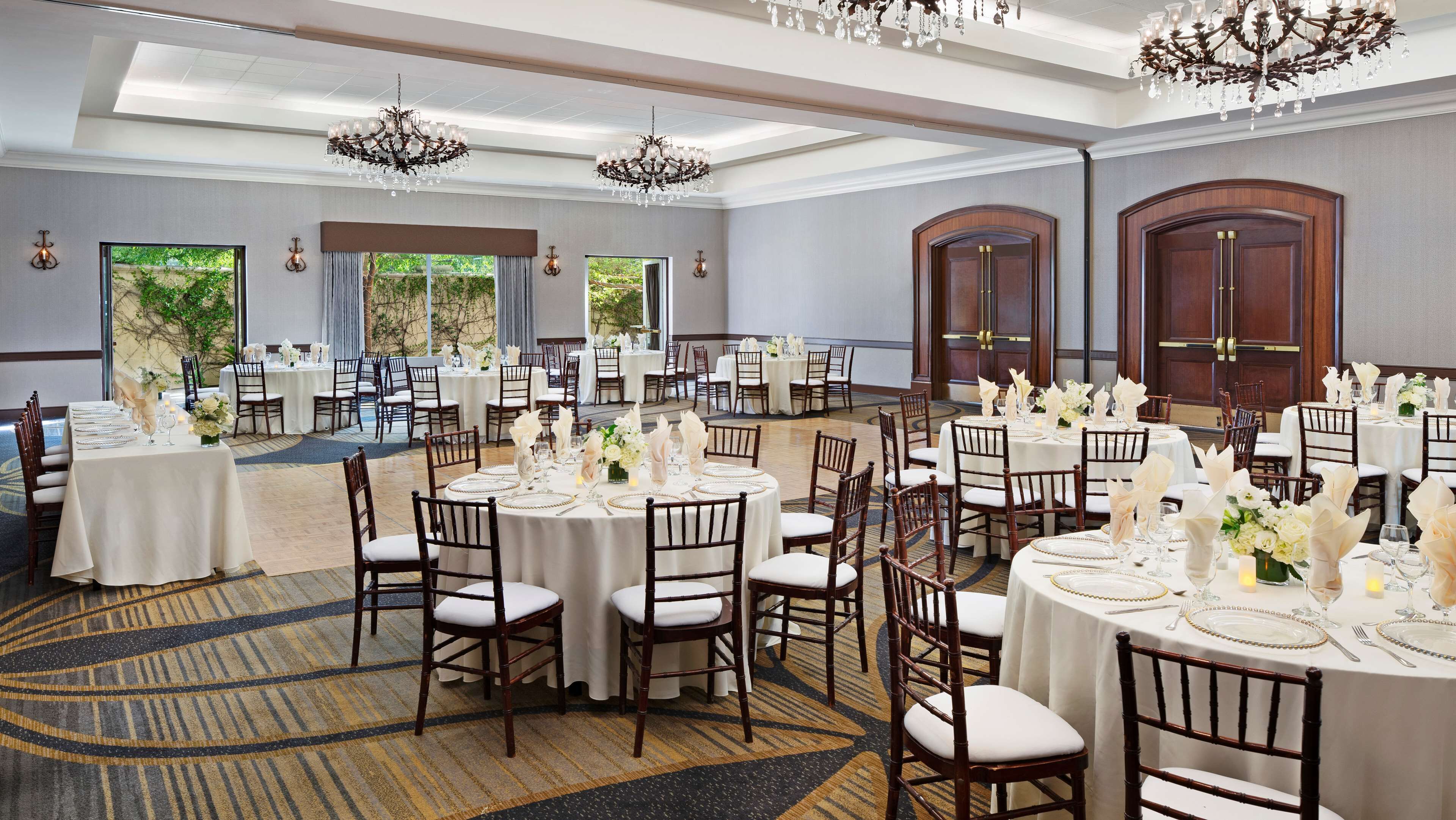 Une salle de banquet avec des tables rondes, des nappes blanches et des chaises en bois.
