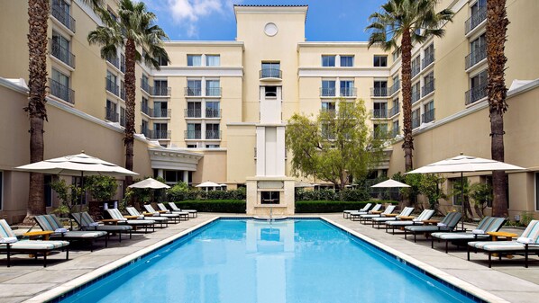 Relax by the rectangular pool surrounded by lounge chairs and umbrellas.
