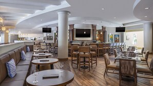 Un hall d’hôtel spacieux avec des tables rondes, des sièges confortables, un bar et un grand écran de télévision.