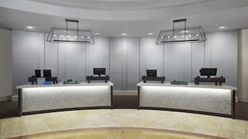 Zona de recepción con dos mostradores, cada uno con una computadora y una planta pequeña. Dos lámparas colgantes iluminan los mostradores, y las paredes están cubiertas de azulejos.