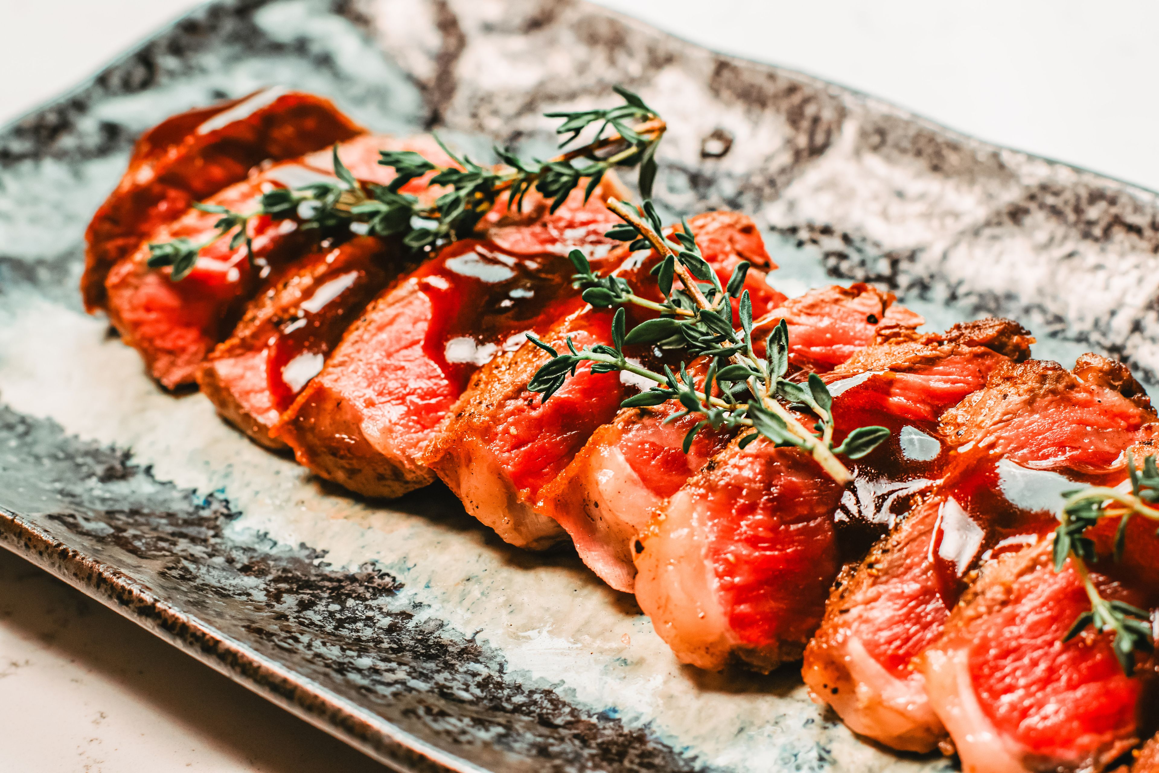 A dish of sliced meat garnished with herbs on a ceramic plate.