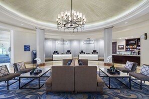 Relax in our spacious lobby, featuring a central seating area with sofas and armchairs, a chandelier, and a reception desk.