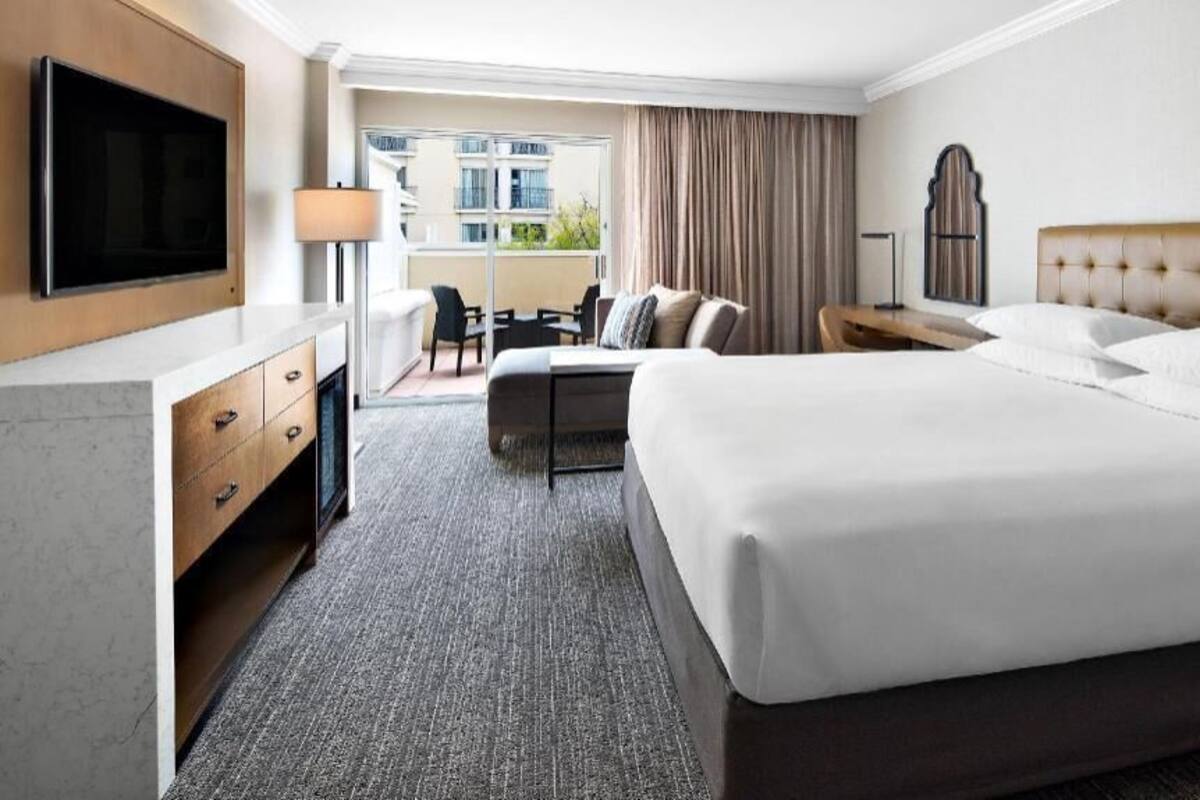 A hotel room with a bed, a desk, a chair, a TV, and a view of the outside.