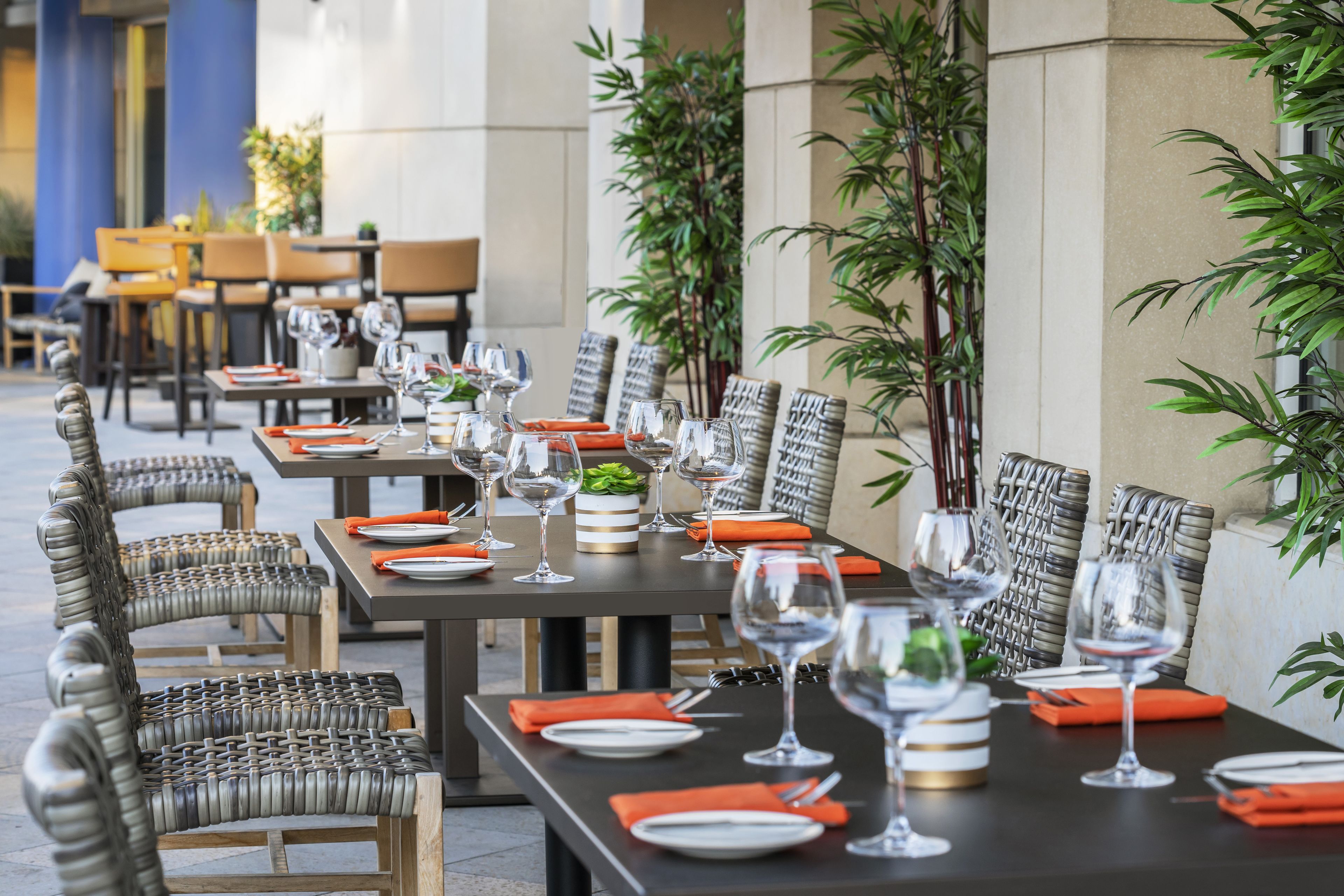 A dining area with tables set for a meal, featuring wicker chairs and a dark tablecloth.