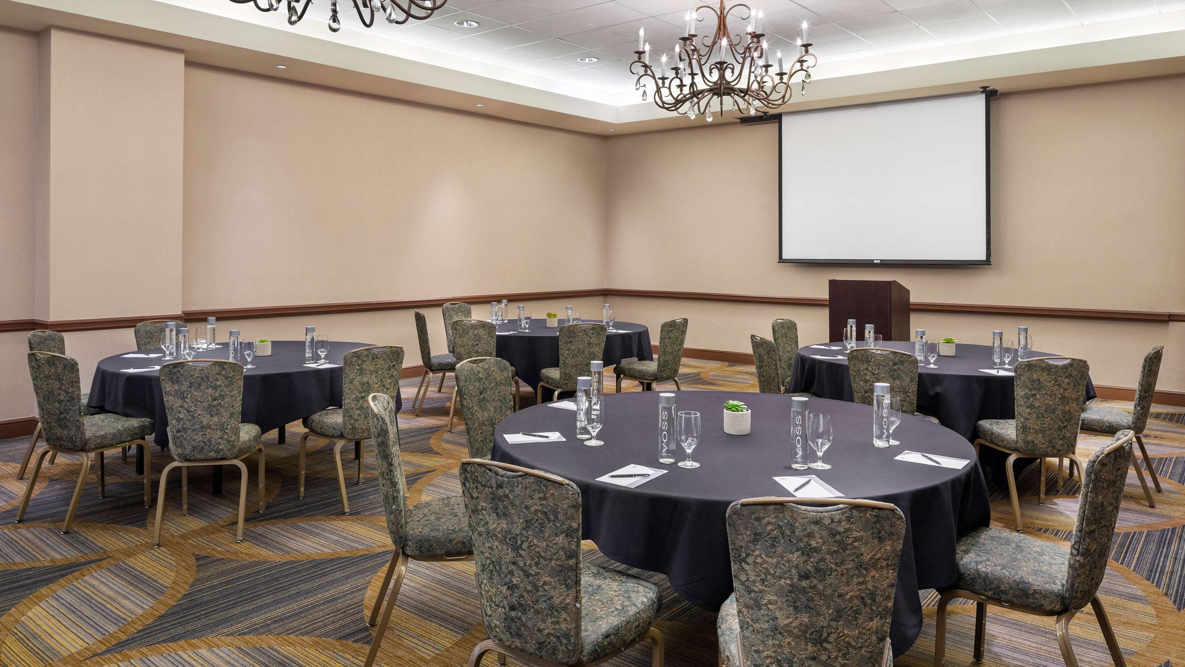 A conference room with round tables, chairs, and a projector screen.