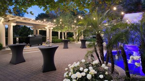 Un espace extérieur aménagé en terrasse, avec des tables et des chaises, un barbecue et une piscine dotée d’un éclairage bleu.