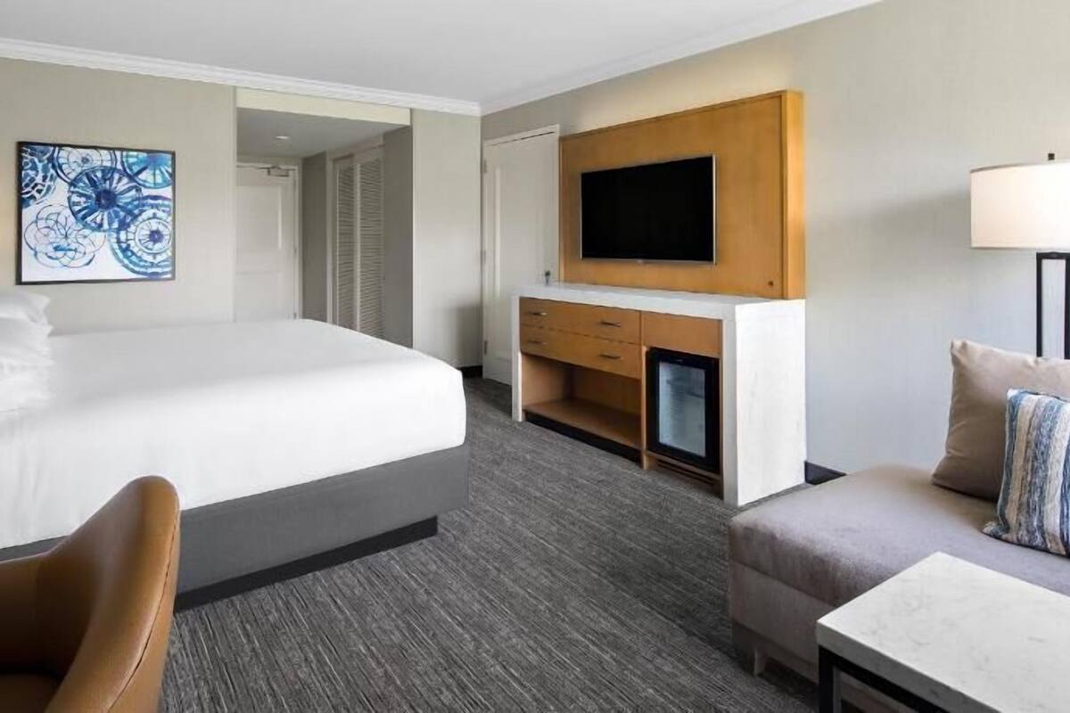 A hotel room with a large bed, a TV mounted on the wall, a desk, and a chair.