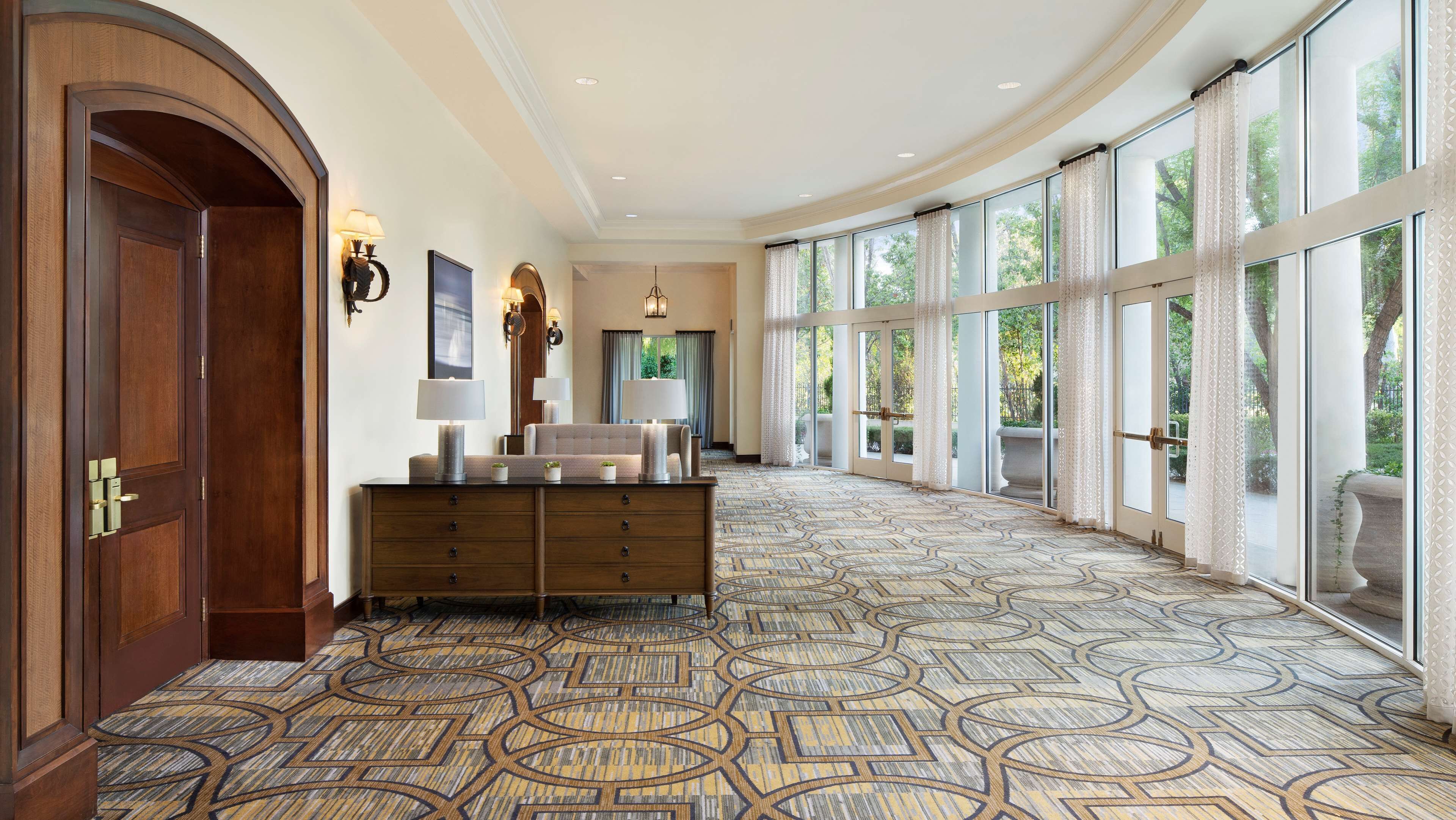 A spacious hallway with a patterned carpet, a wooden bench, and a large window with curtains.