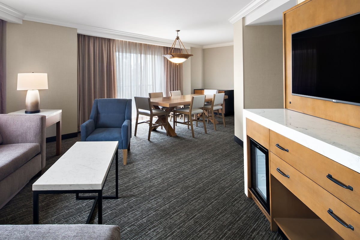 Ein Hotelzimmer mit einer Couch, einem Esstisch mit Stühlen, einem Fernseher und einer Lampe.