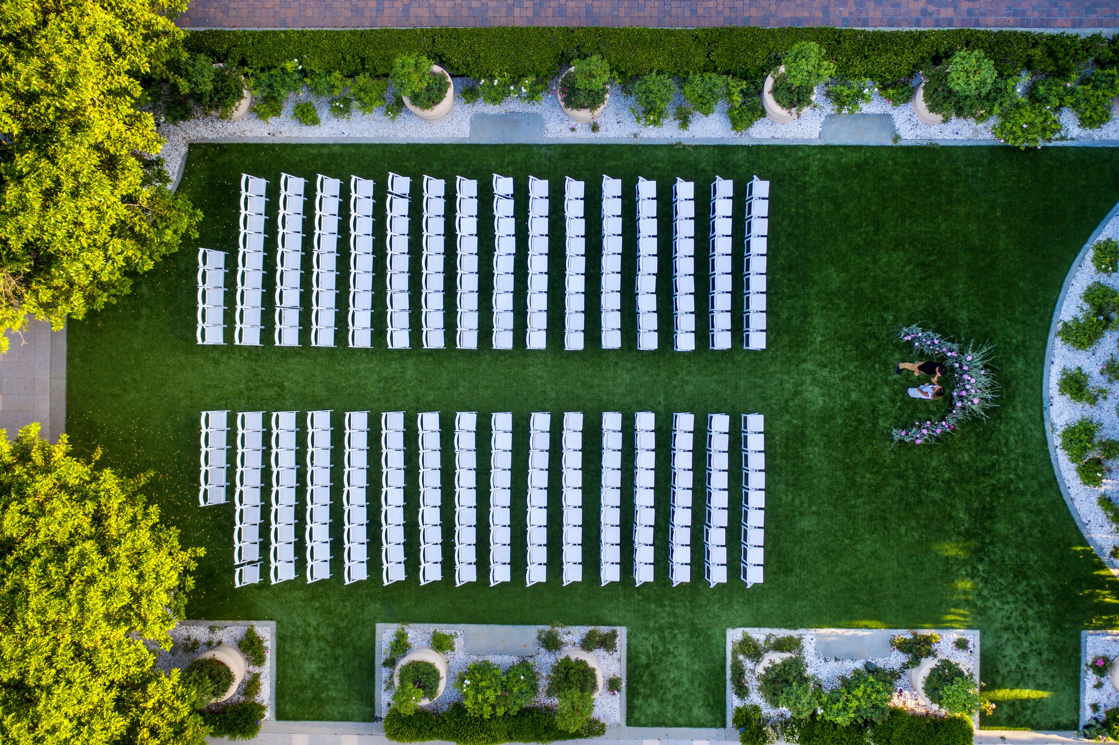 An aerial view of a hotel courtyard with rows of white tables and chairs, surrounded by greenery and pathways.