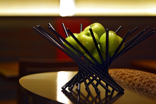 Una mesa con un soporte metálico negro para manzanas que contiene tres manzanas verdes.
