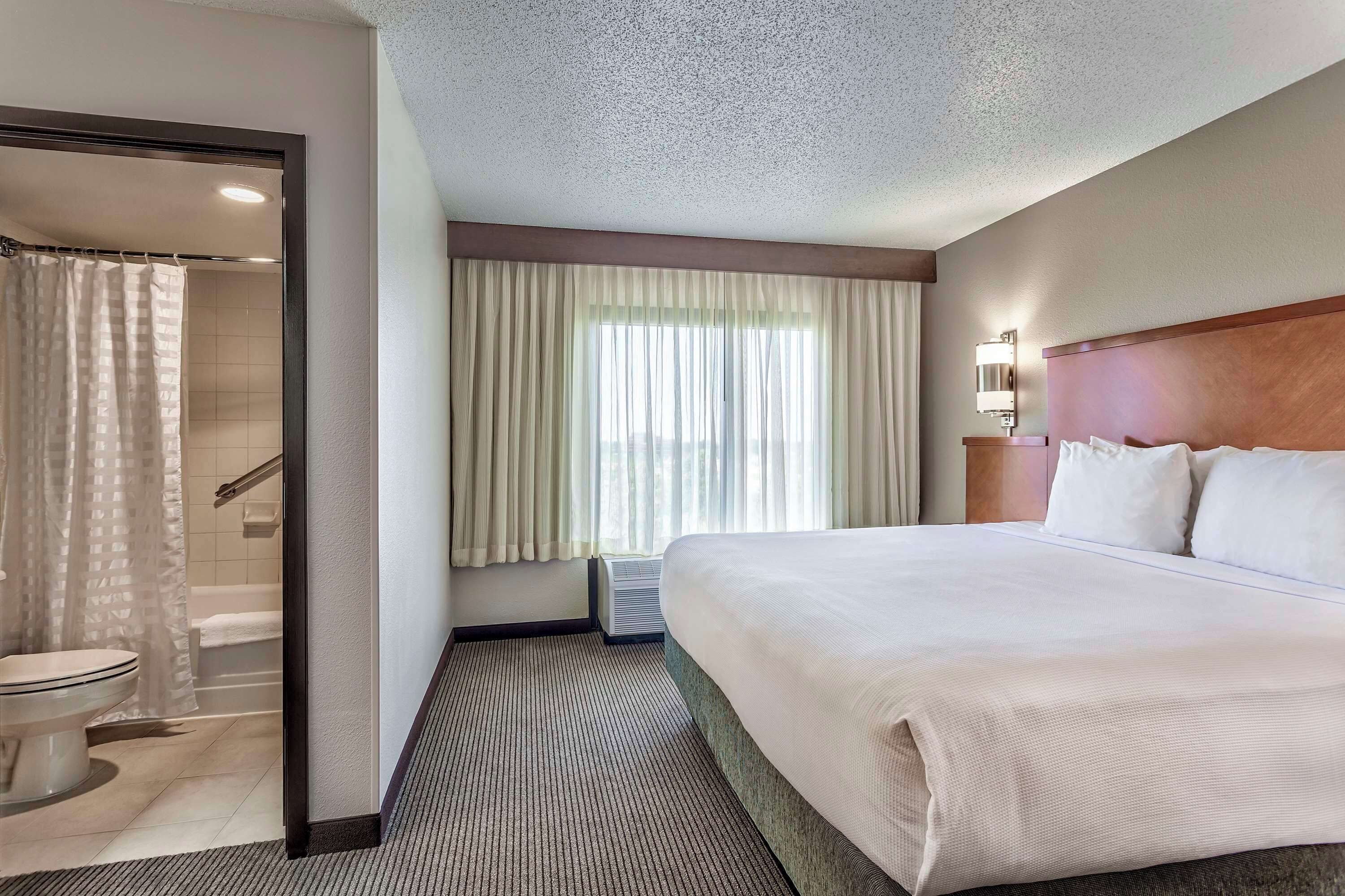 A hotel room with a large bed, a shower area, and a window with curtains.