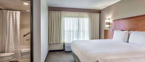 A hotel room with a large bed, a shower area, and a window with curtains.