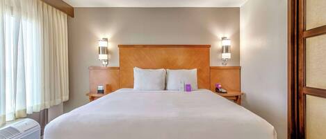 Ein Hotelzimmer mit einem großen Bett, zwei Nachttischen mit Lampen, einem Fenster mit Vorhängen und einem an der Wand montierten Heizkörper.