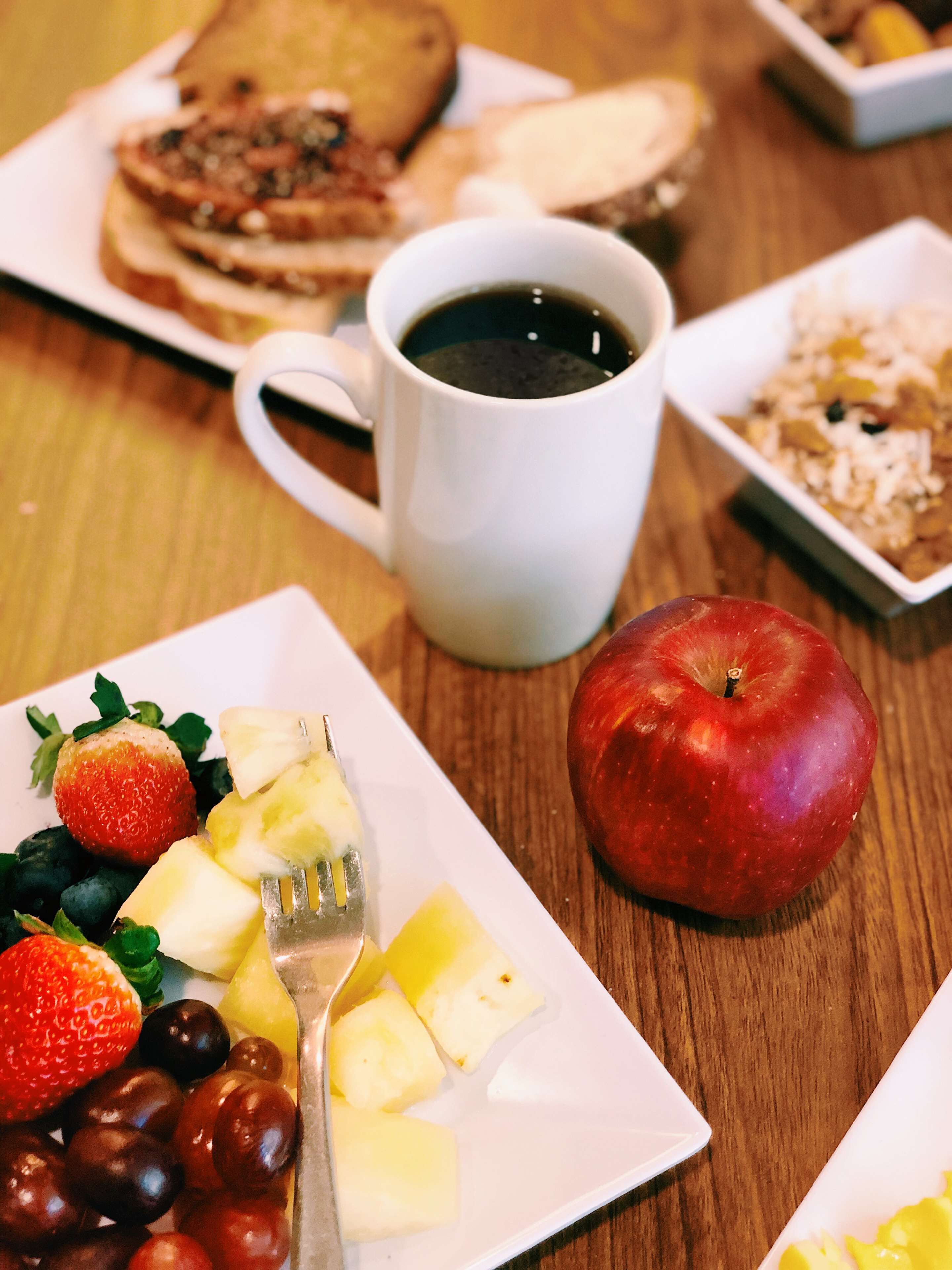 Une table mise pour le petit-déjeuner avec une assiette de fruits, une tasse de café et une tranche de pain grillé.