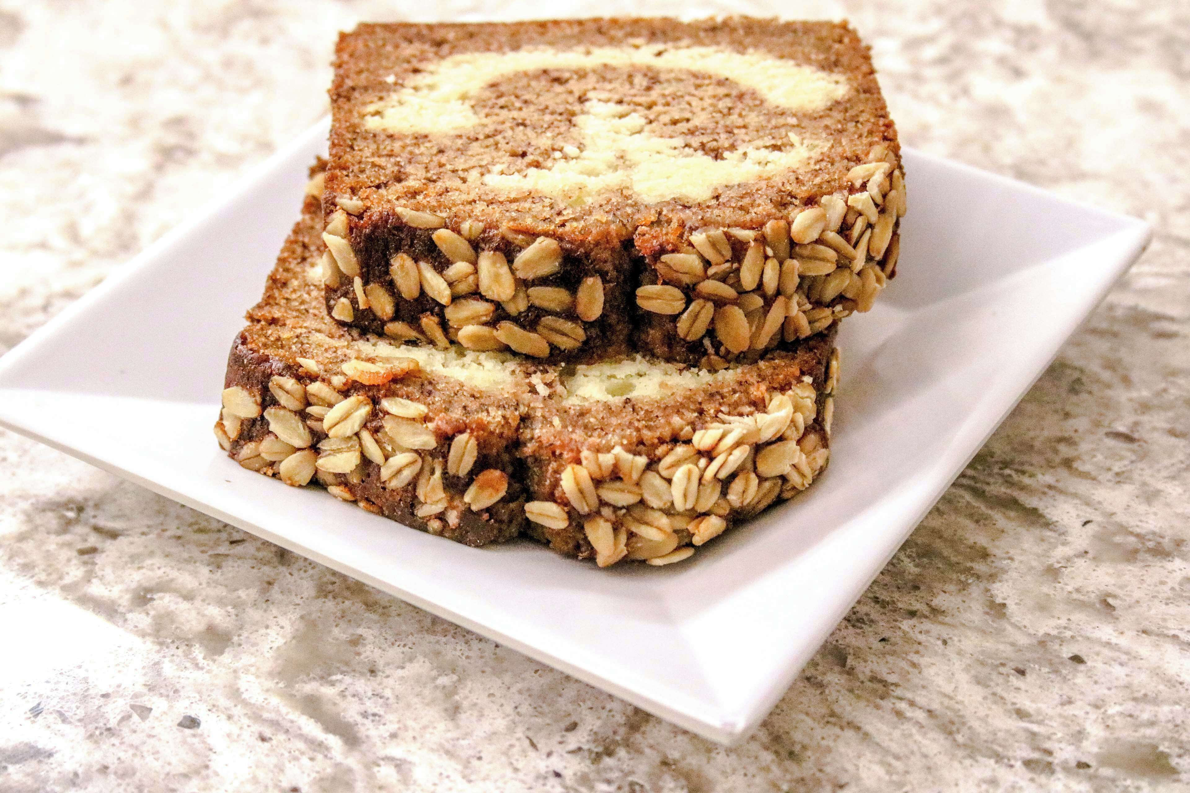 A stack of square-shaped, multi-layered bars topped with seeds, placed on a white rectangular plate.