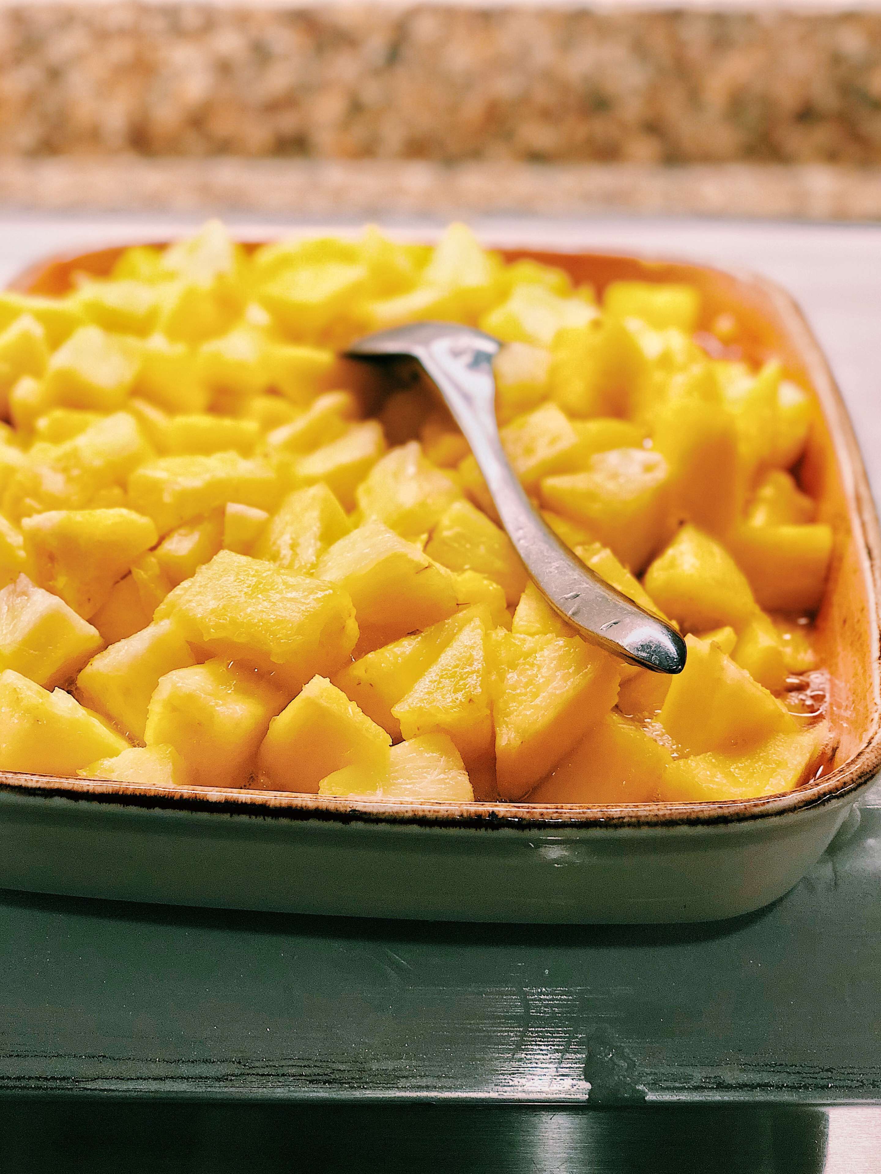 A rectangular baking dish filled with diced yellow fruit, possibly pineapple, with a spoon inside.