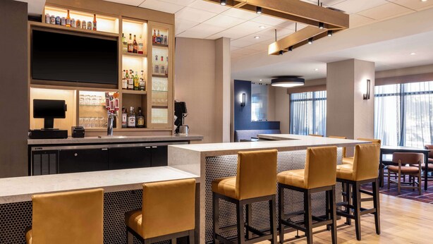 A modern hotel lobby with a bar area, seating, and a large TV screen. - Hyatt Place Kansas City/Overland Park/Convention Center (Overland Park)
