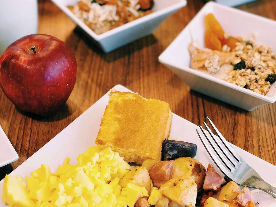 Una mesa de desayuno con diversos platos, incluyendo huevos, tocino, tostadas y fruta.
