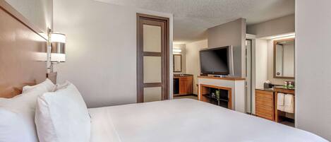 A hotel room with a large bed, a television, a desk with a mirror, and a bathroom with a sink and toilet.